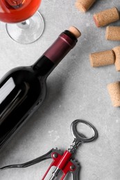 Photo of Wine corks, bottle, glass of drink and corkscrew on light grey table, flat lay