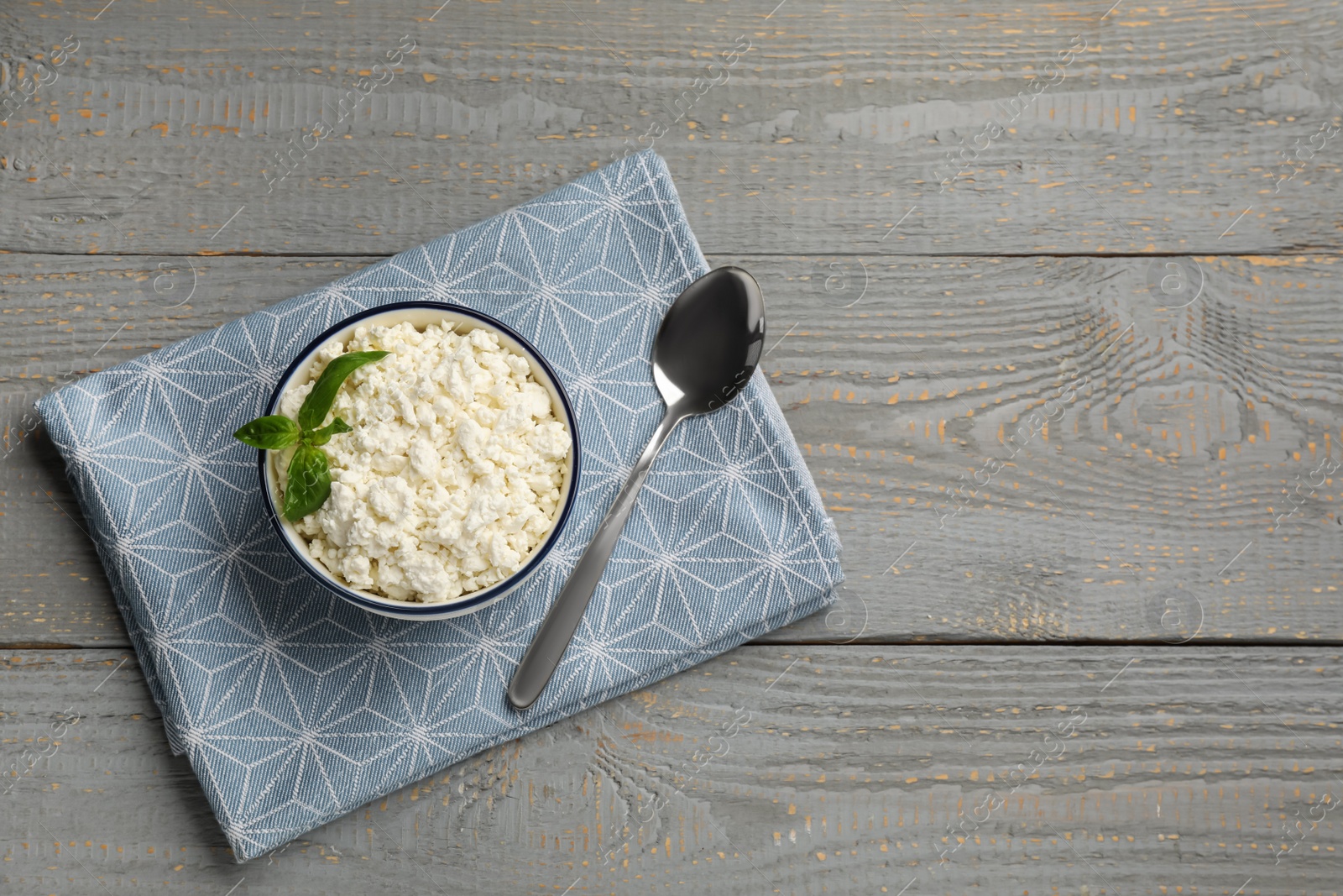 Photo of Delicious fresh cottage cheese with basil on grey wooden table, flat lay. Space for text