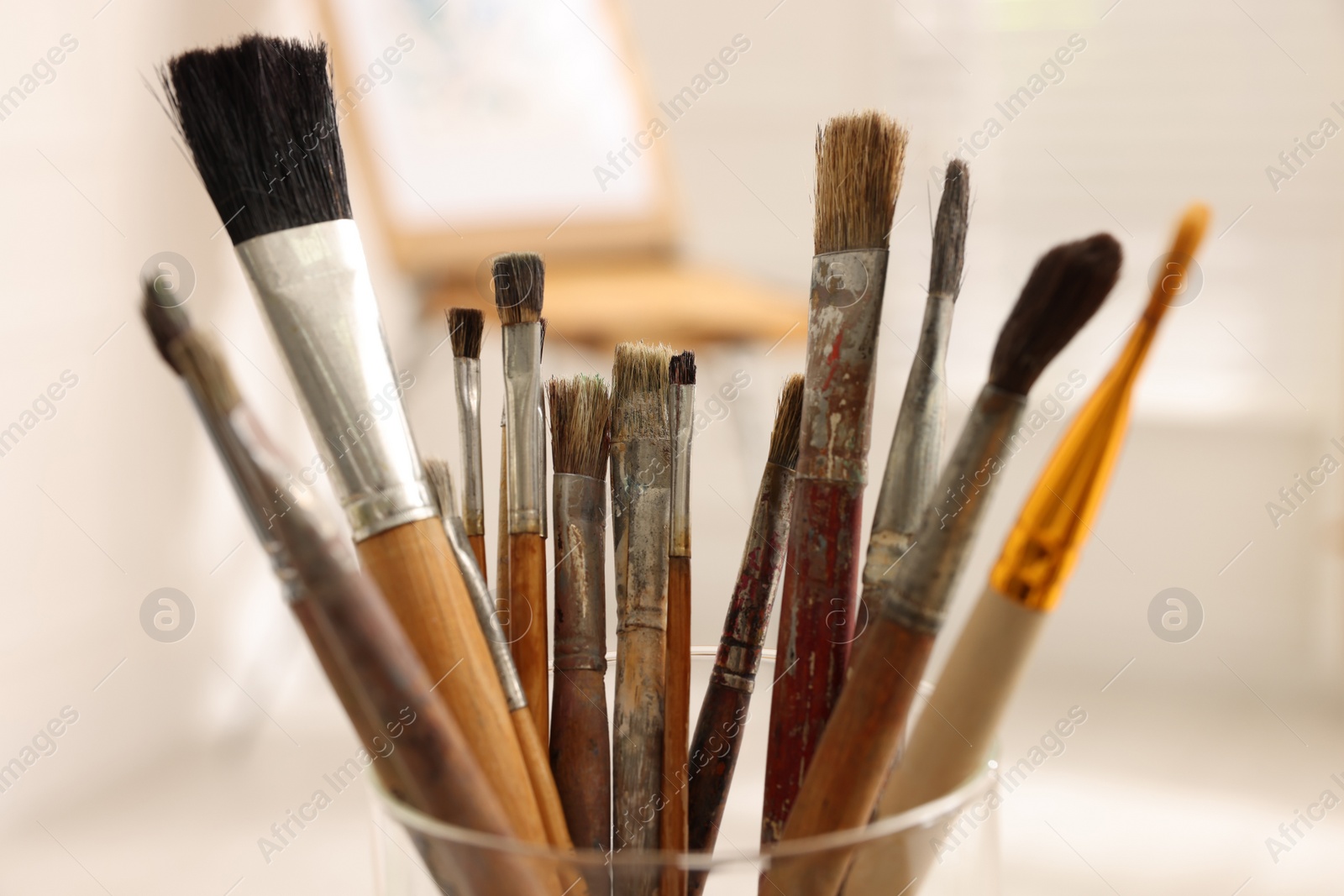 Photo of Glass holder with different paintbrushes indoors, closeup