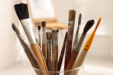 Glass holder with different paintbrushes indoors, closeup