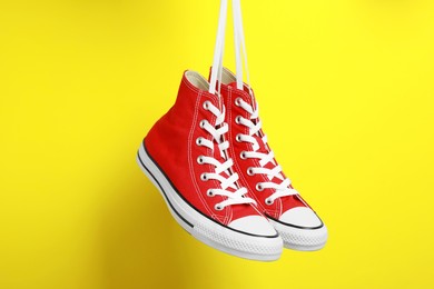 Pair of new stylish red sneakers hanging on laces against yellow background