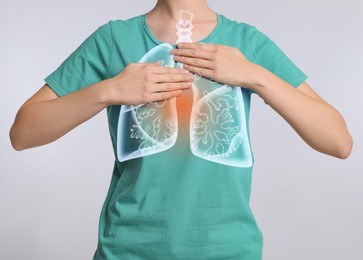Woman holding hands near chest with illustration of lungs on light grey background, closeup