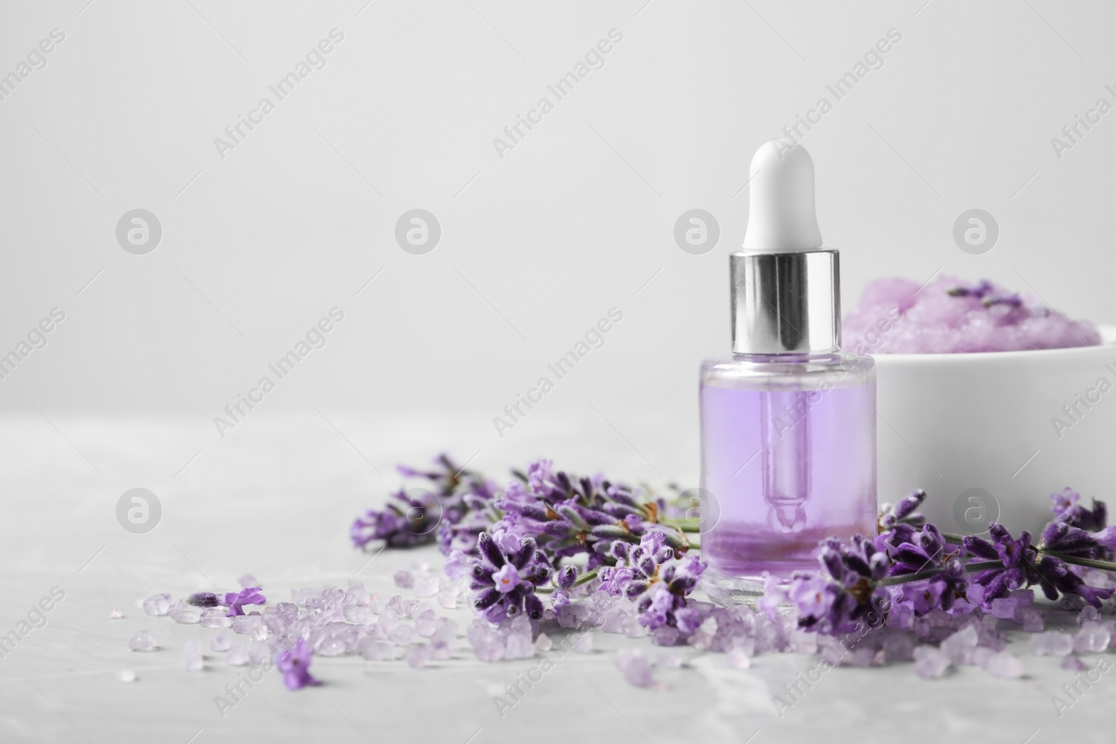 Photo of Natural cosmetic oil, bath salt, scrub and lavender flowers on grey marble table, space for text