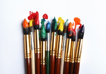 Brushes with colorful paints on white background, flat lay