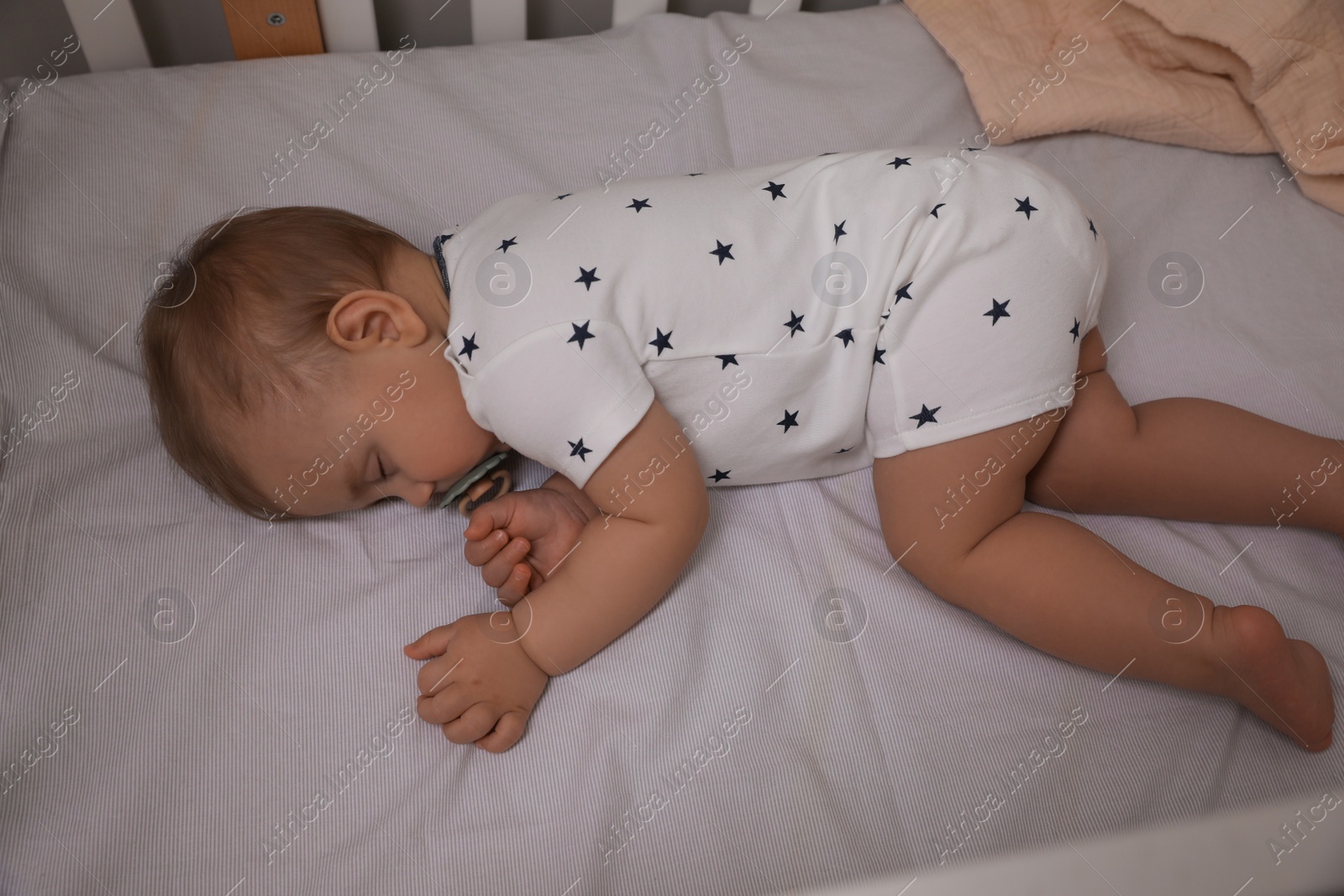 Photo of Adorable little baby with pacifier sleeping in crib, above view