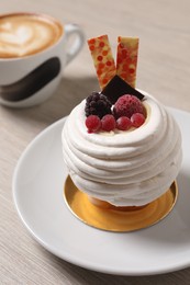 Photo of Delicious meringue dessert with berries and cup of coffee on wooden table, closeup