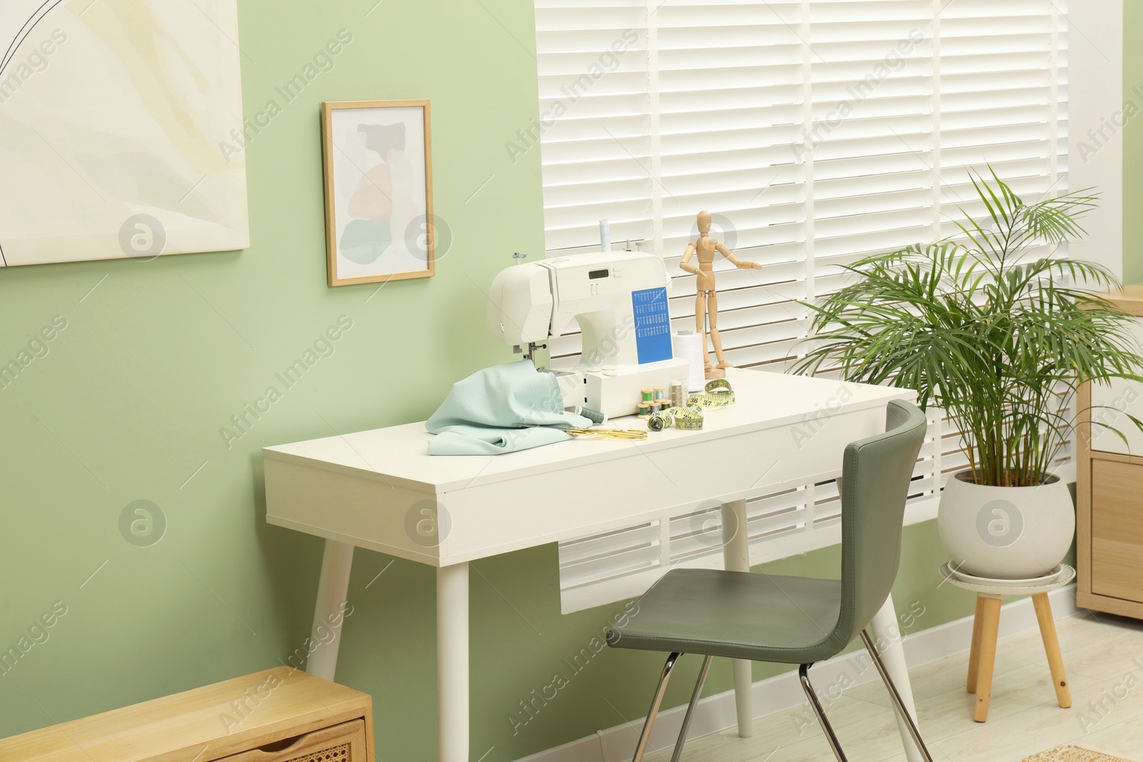 Photo of Modern sewing machine with cloth and craft accessories on white table near window in room