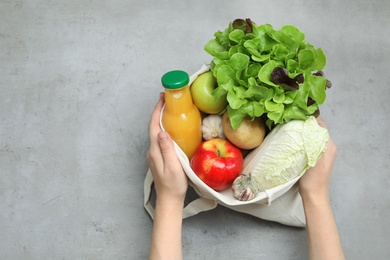 Photo of Woman holding bag with fresh vegetables, apples and bottle of juice on color background, top view. Space for text