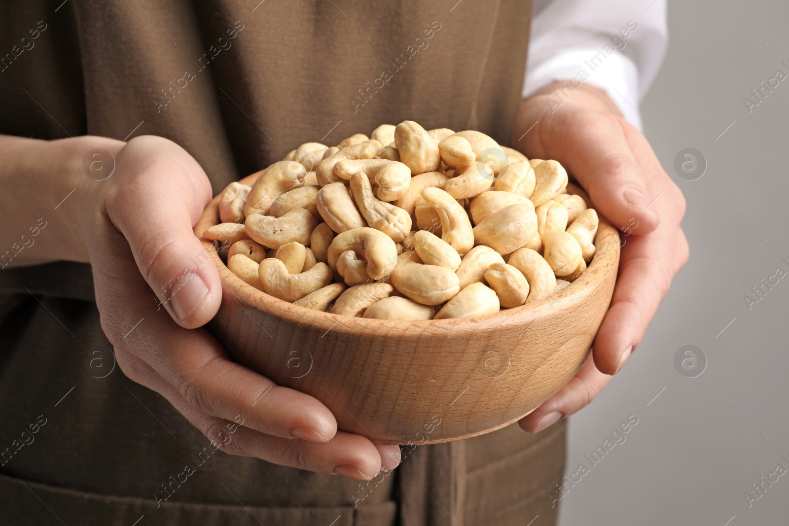 Photo of Woman holding bowl of cashew nuts on light background, closeup