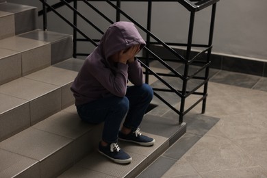 Photo of Child abuse. Upset boy sitting on stairs indoors