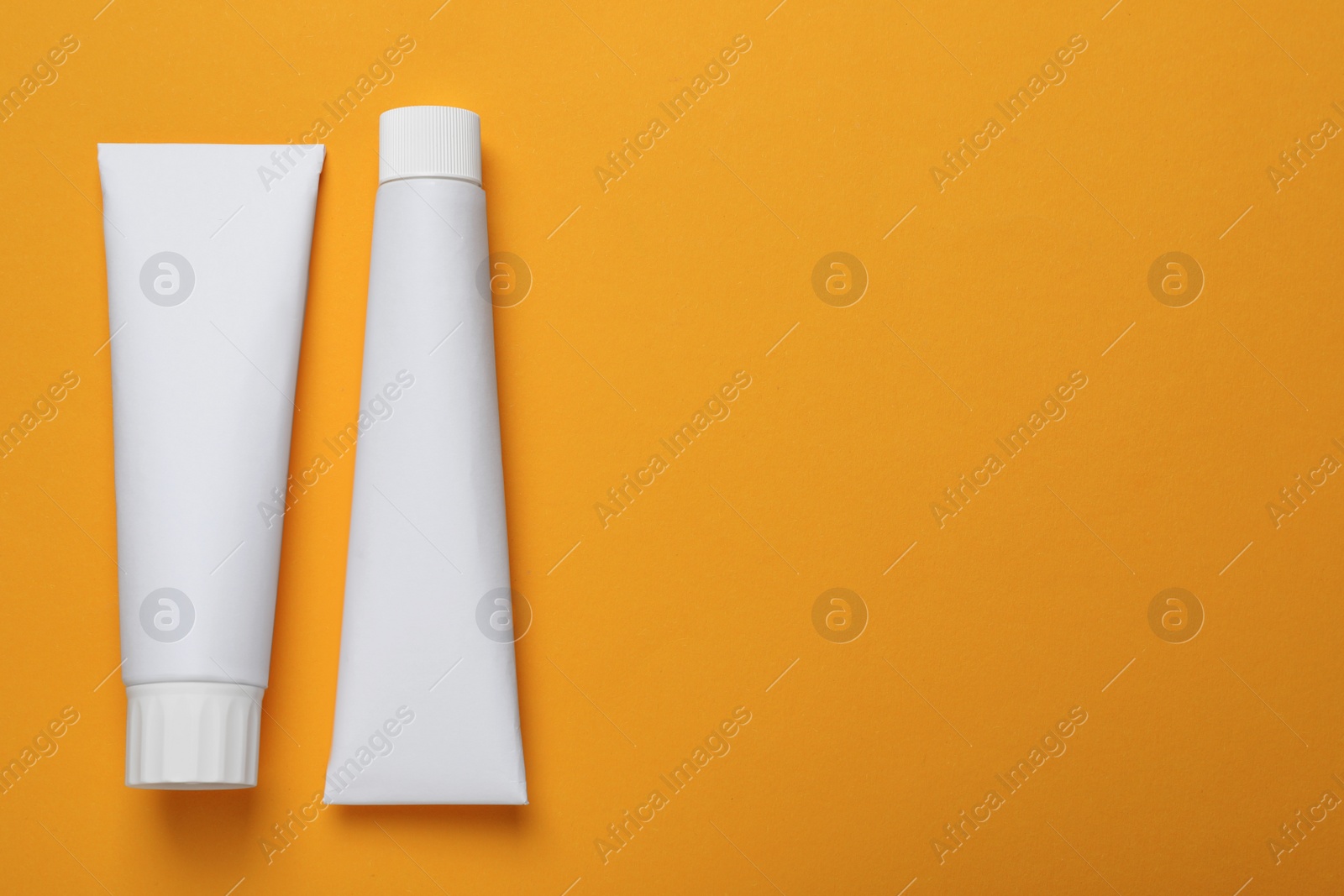 Photo of Blank tubes of toothpaste on orange background, flat lay. Space for text