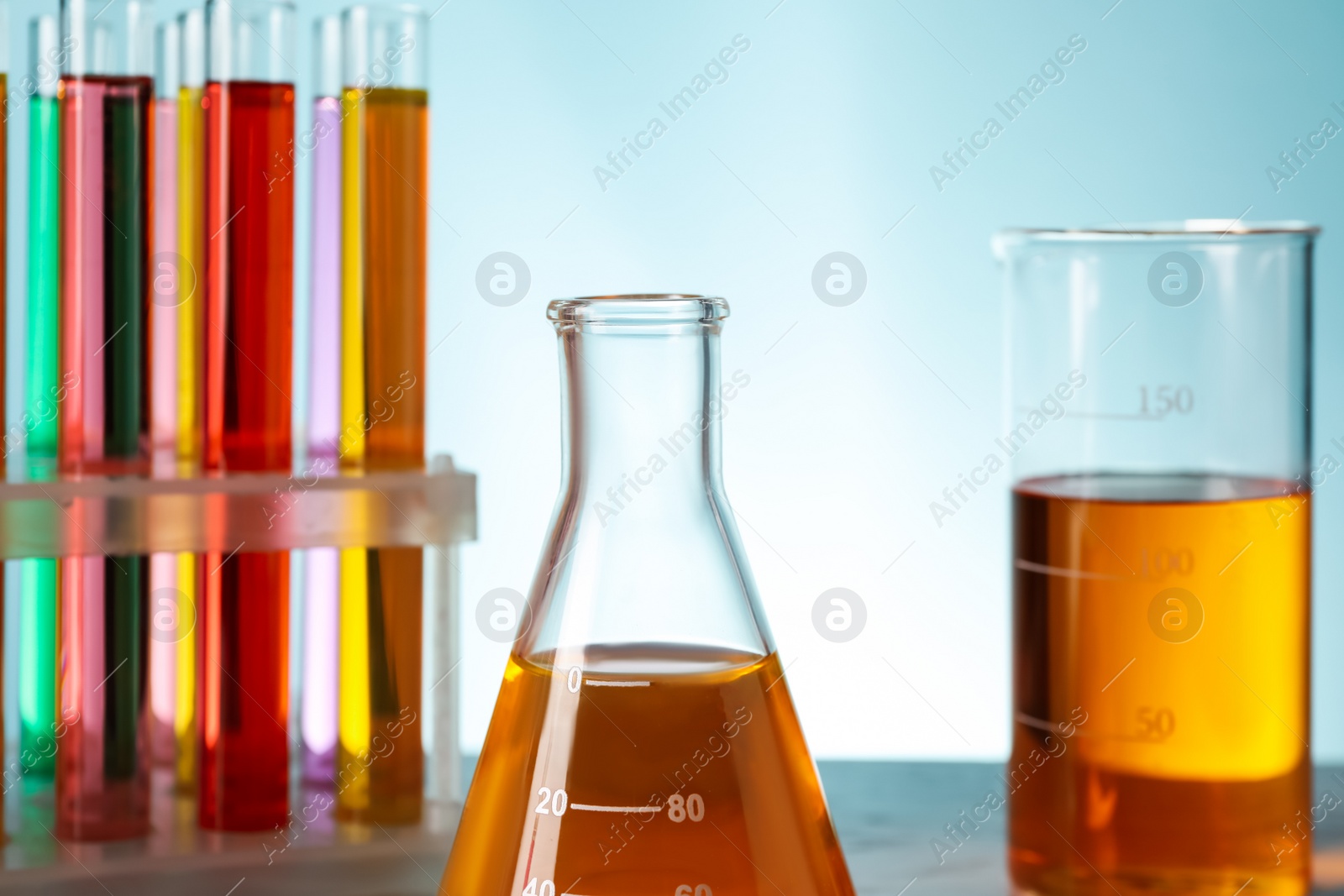 Photo of Different laboratory glassware with colorful liquids on turquoise background, closeup