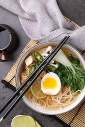 Photo of Bowl of vegetarian ramen, soy sauce and chopsticks on grey table, flat lay