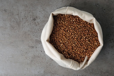 Photo of Uncooked buckwheat in sackcloth bag on grey background, top view. Space for text