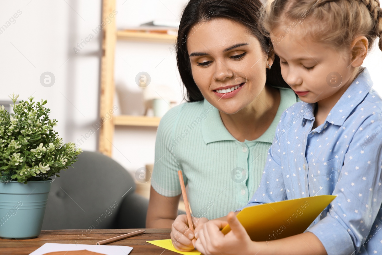 Photo of Cute little girl with her mother making beautiful greeting card at home