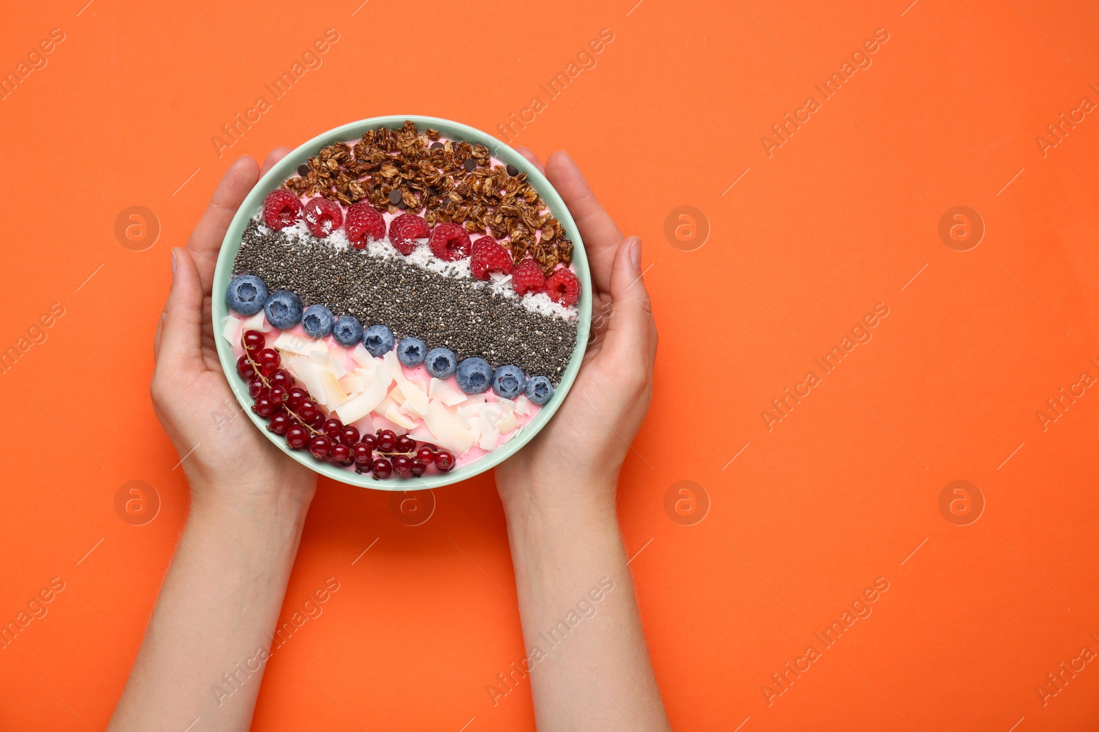 Photo of Woman holding bowl of tasty smoothie with fresh berries and granola on orange background, top view. Space for text