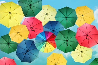 Image of Group of different colorful umbrellas against blue sky on sunny day