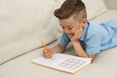 Little boy solving sudoku puzzle on sofa at home