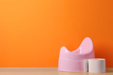 Photo of Pink baby potty and toilet paper on wooden table against orange background, space for text