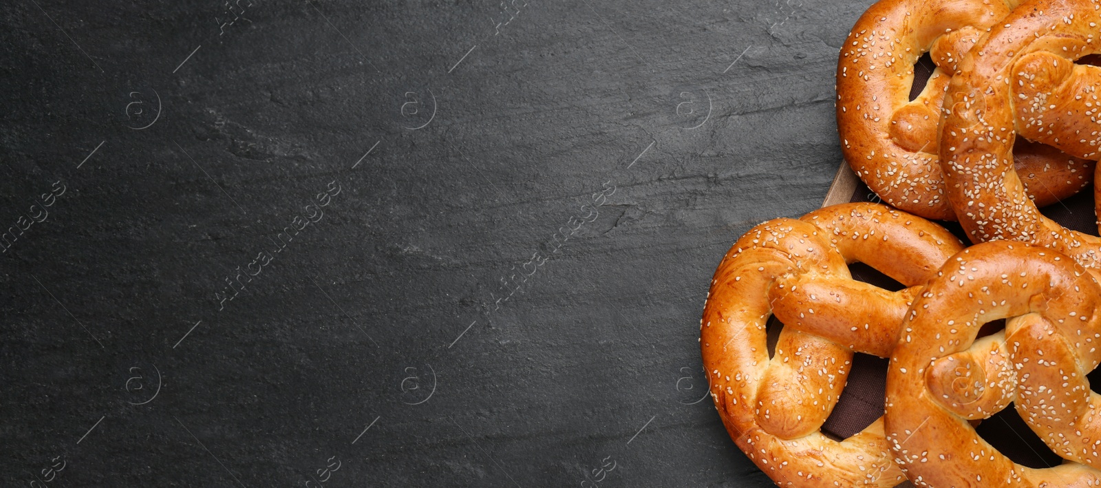 Image of Delicious pretzels with sesame seeds on black table, top view with space for text. Banner design