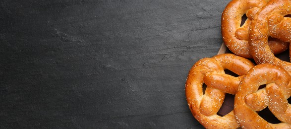 Image of Delicious pretzels with sesame seeds on black table, top view with space for text. Banner design