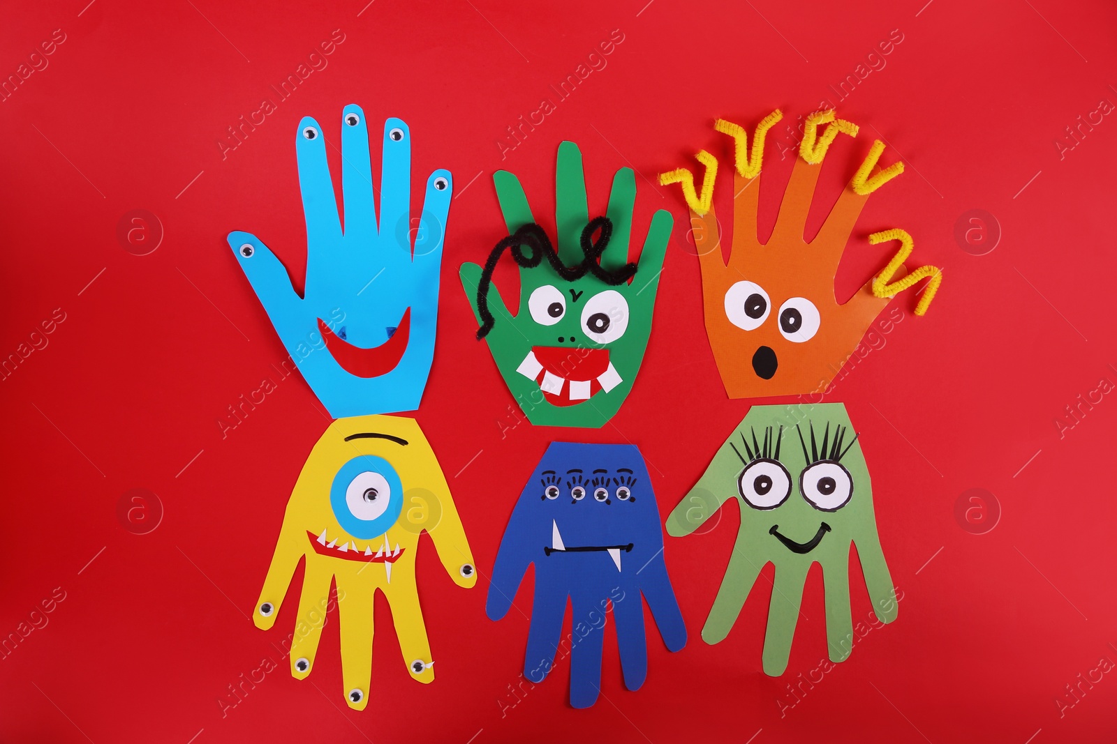 Photo of Funny hand shaped monsters on red background, flat lay. Halloween decoration