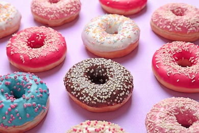 Delicious glazed doughnuts with sprinkles on color background