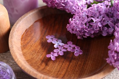 Photo of Bowl of water and lilac flowers on wooden table, closeup