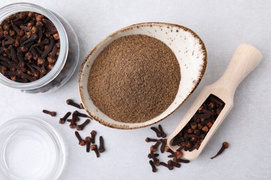 Aromatic clove powder, scoop and dried buds on light table, flat lay