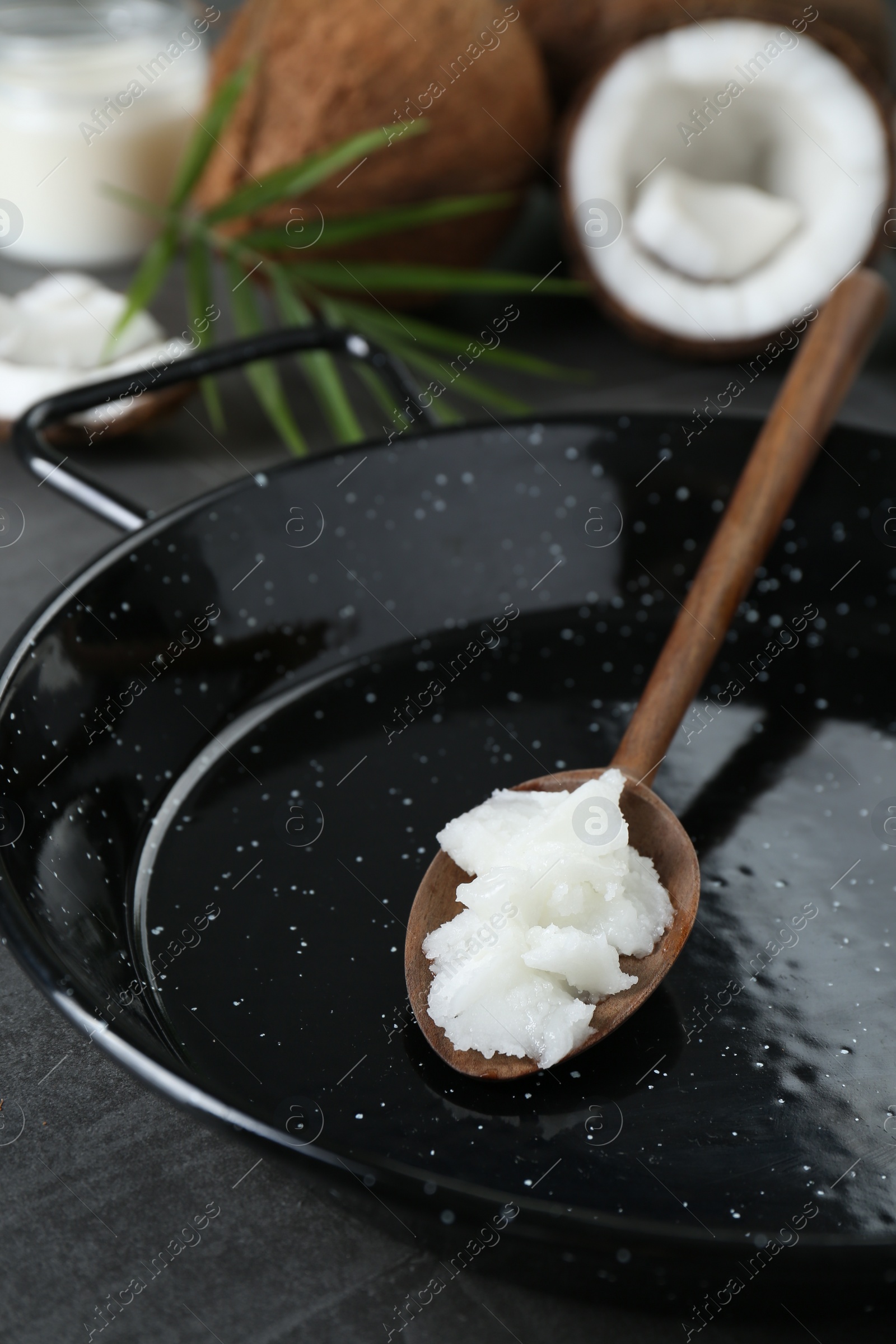 Photo of Frying pan with organic coconut cooking oil and wooden spoon on grey table