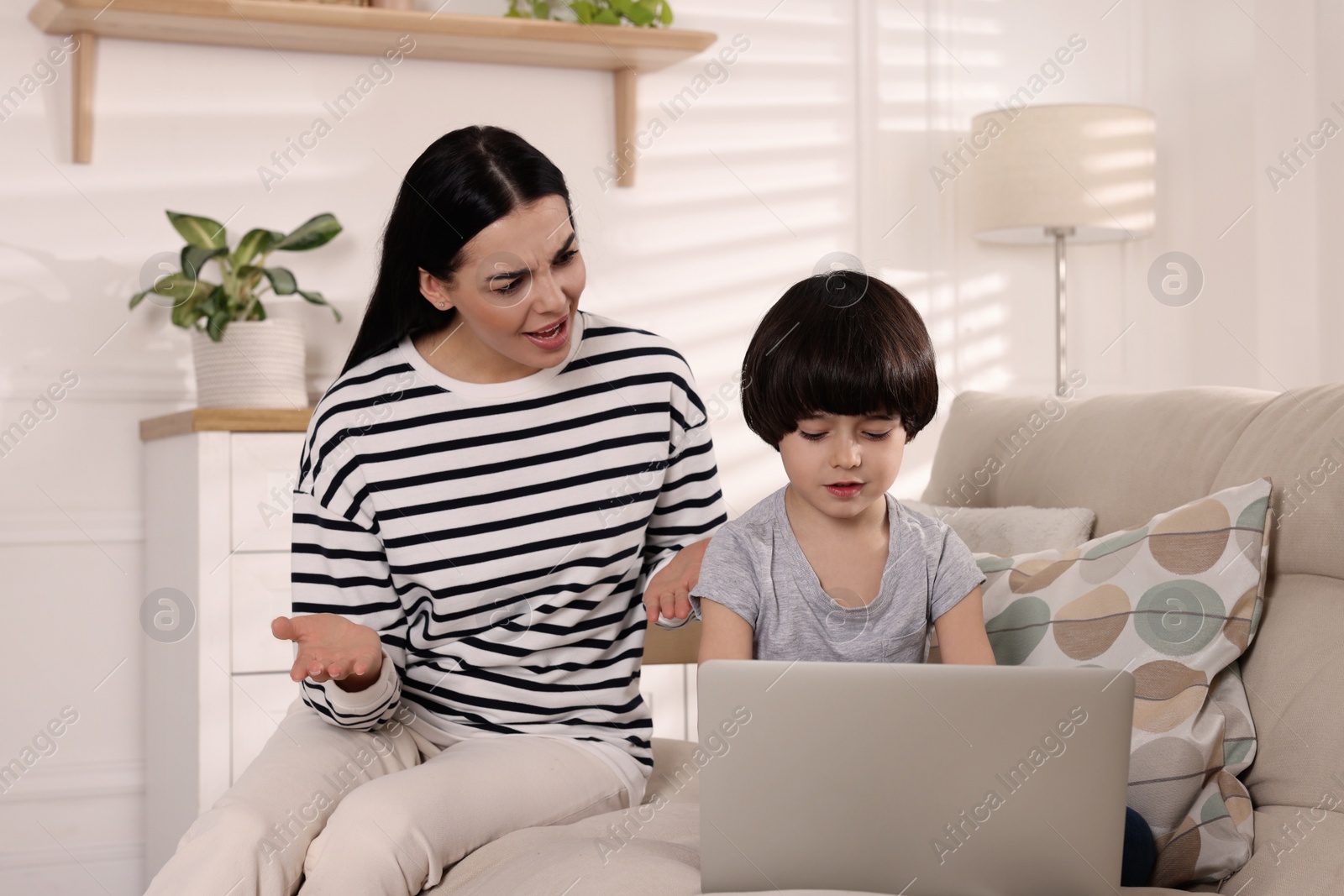 Photo of Internet addiction. Woman scolding her son while he using laptop in living room