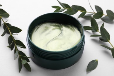 Photo of Under eye patches in jar near green twigs on white background, closeup. Cosmetic product
