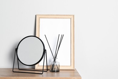Photo of Stylish mirror, reed diffuser and picture frame on table near light wall