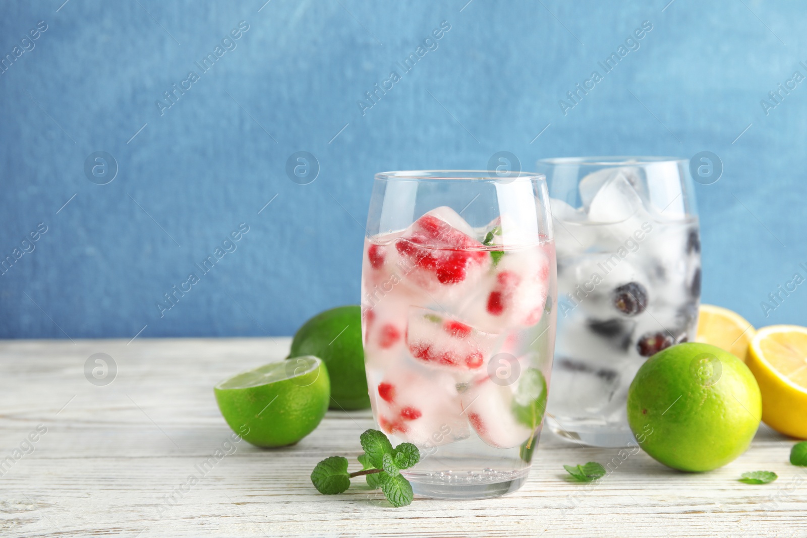 Photo of Glasses of drinks with fruit ice cubes on table against color background. Space for text