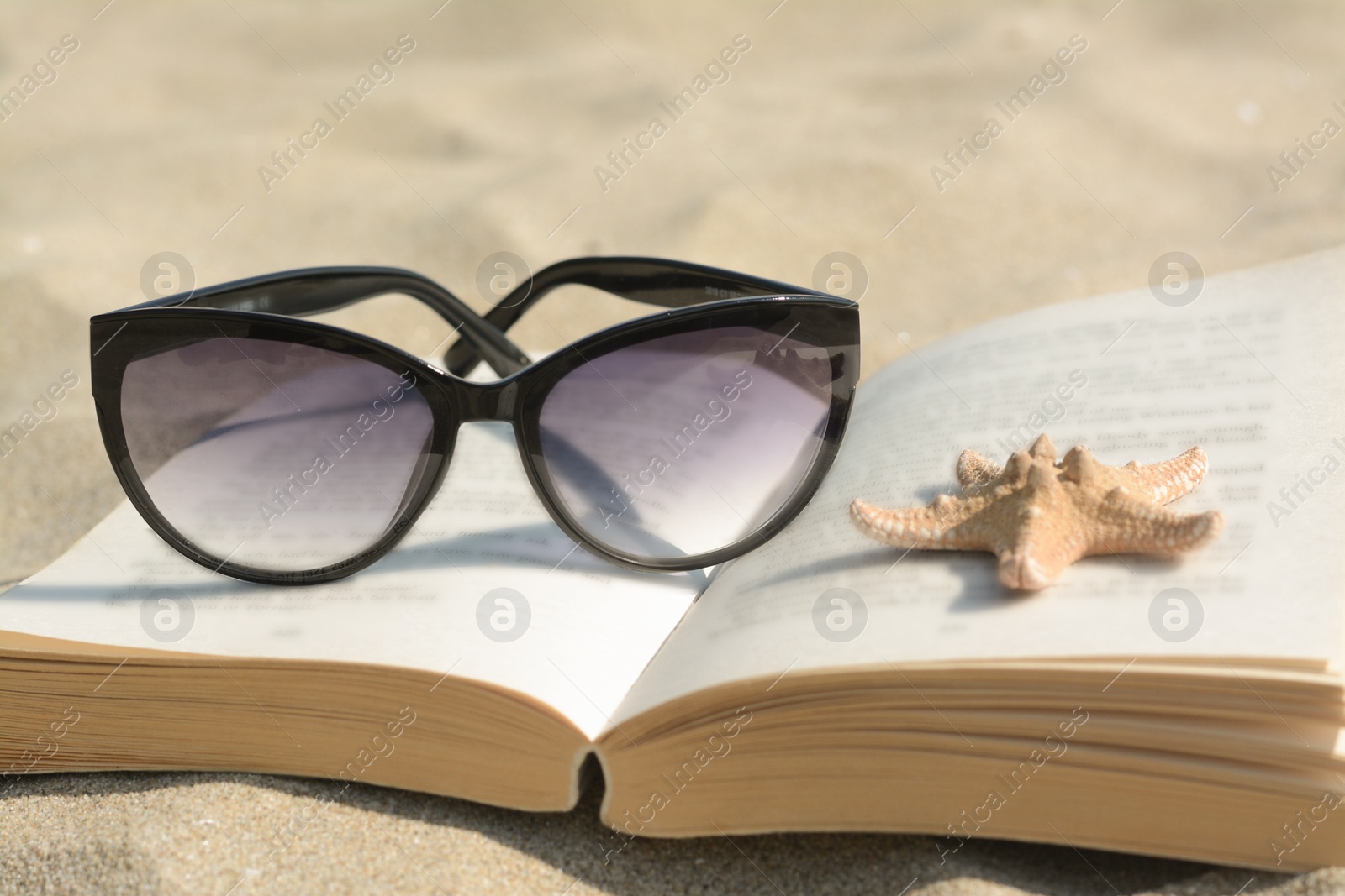Photo of Beautiful sunglasses, book and starfish on sand, closeup