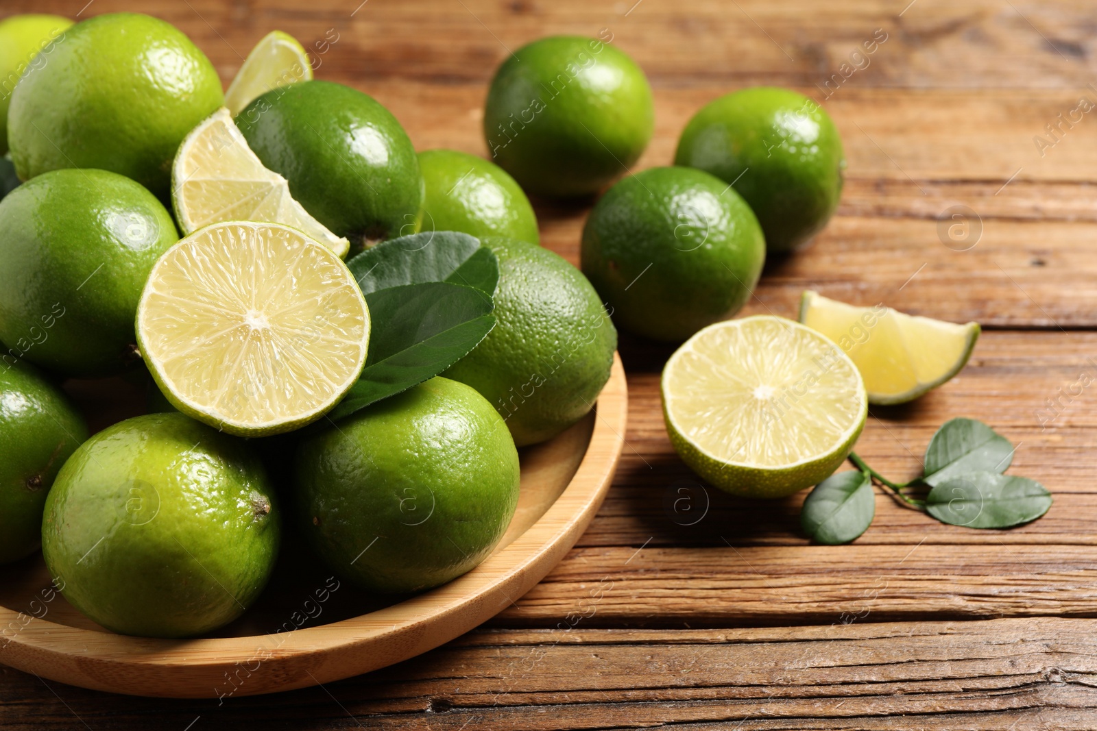 Photo of Fresh ripe limes and green leaves on wooden table