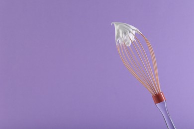 Whisk with whipped cream on violet background. Space for text