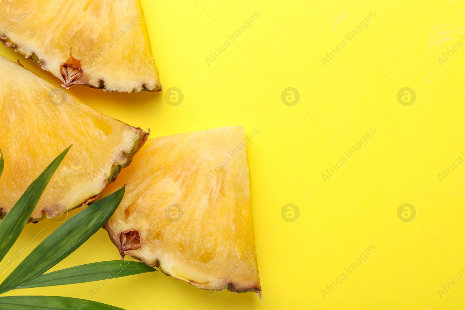 Photo of Pieces of tasty ripe pineapple and green leaves on yellow background, flat lay. Space for text