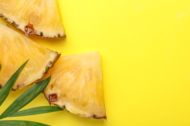 Pieces of tasty ripe pineapple and green leaves on yellow background, flat lay. Space for text