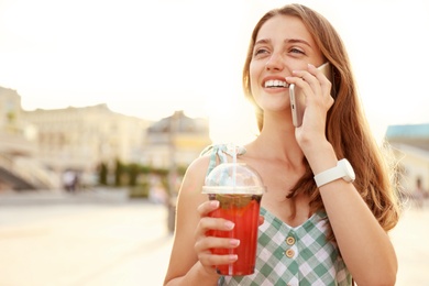 Photo of Young woman with refreshing drink talking on phone outdoors. Space for text