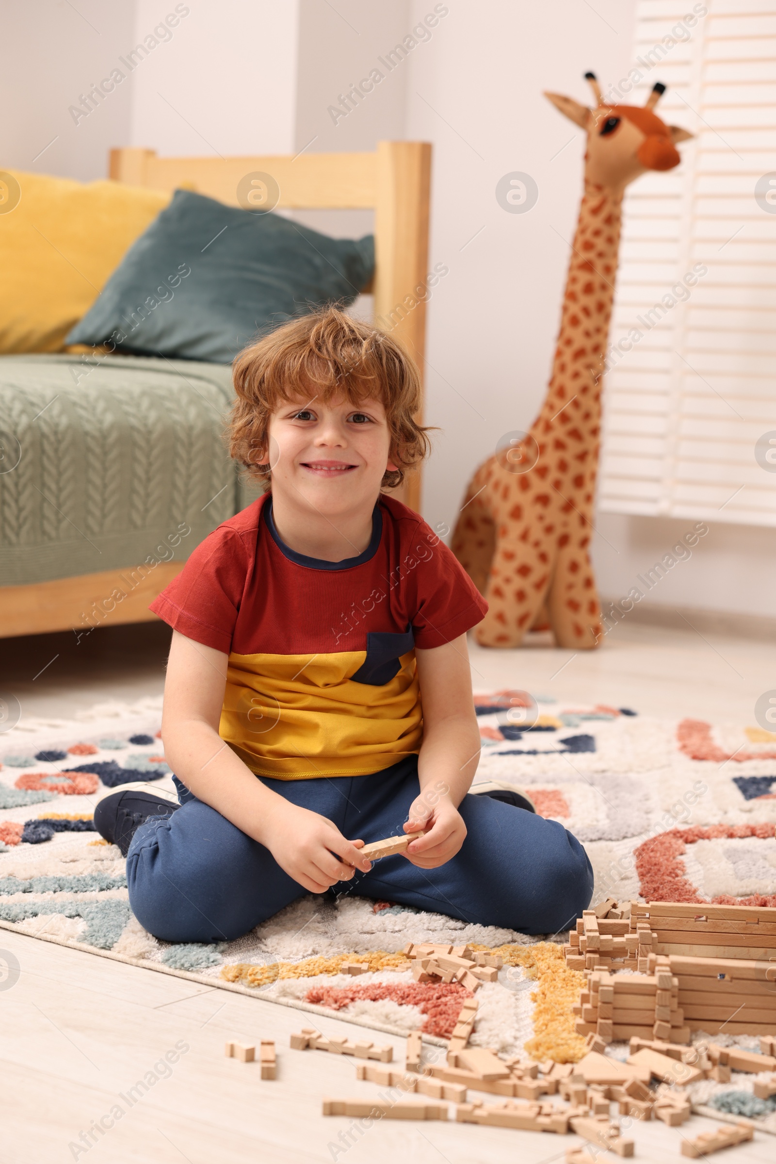 Photo of Little boy playing with wooden construction set on carpet in room. Child's toy