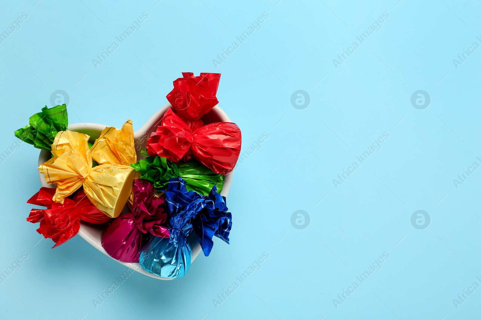 Photo of Candies in colorful wrappers on light blue background, top view. Space for text