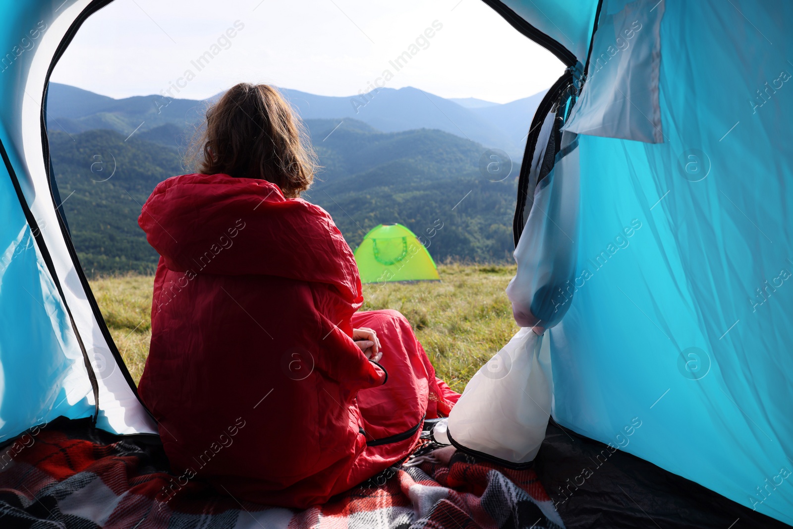 Photo of Mature woman in sleeping bag looking outside of camping tent, back view