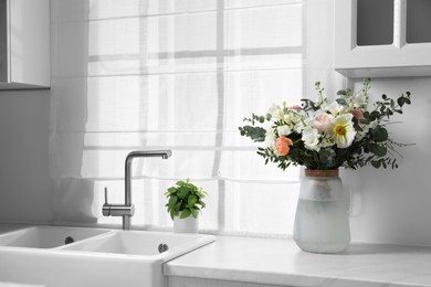 Bouquet of beautiful flowers on white countertop in kitchen