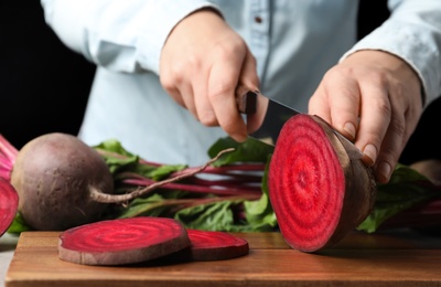 Woman cutting fresh red beet at table, closeup