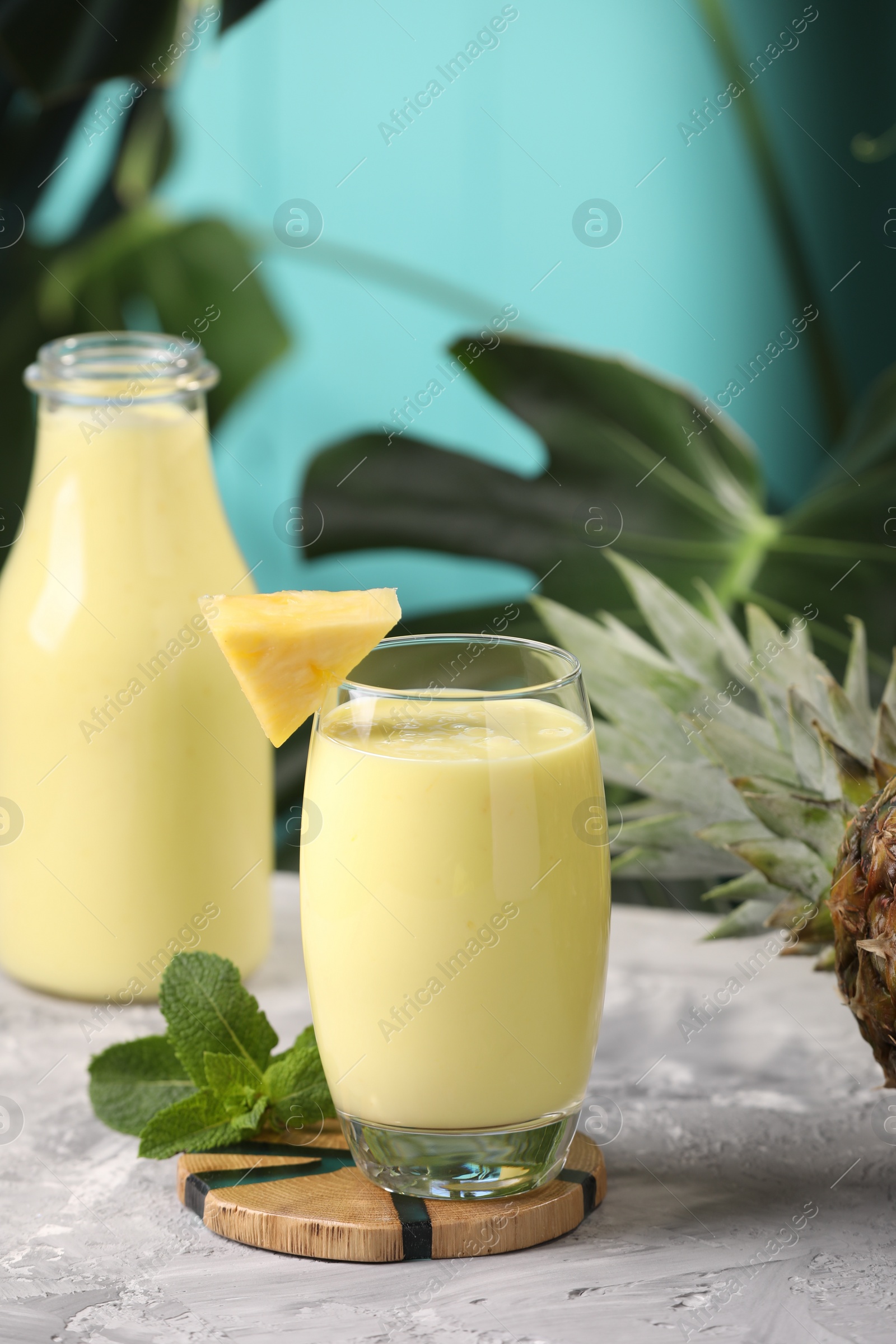 Photo of Tasty pineapple smoothie, mint and fruit on grey textured table