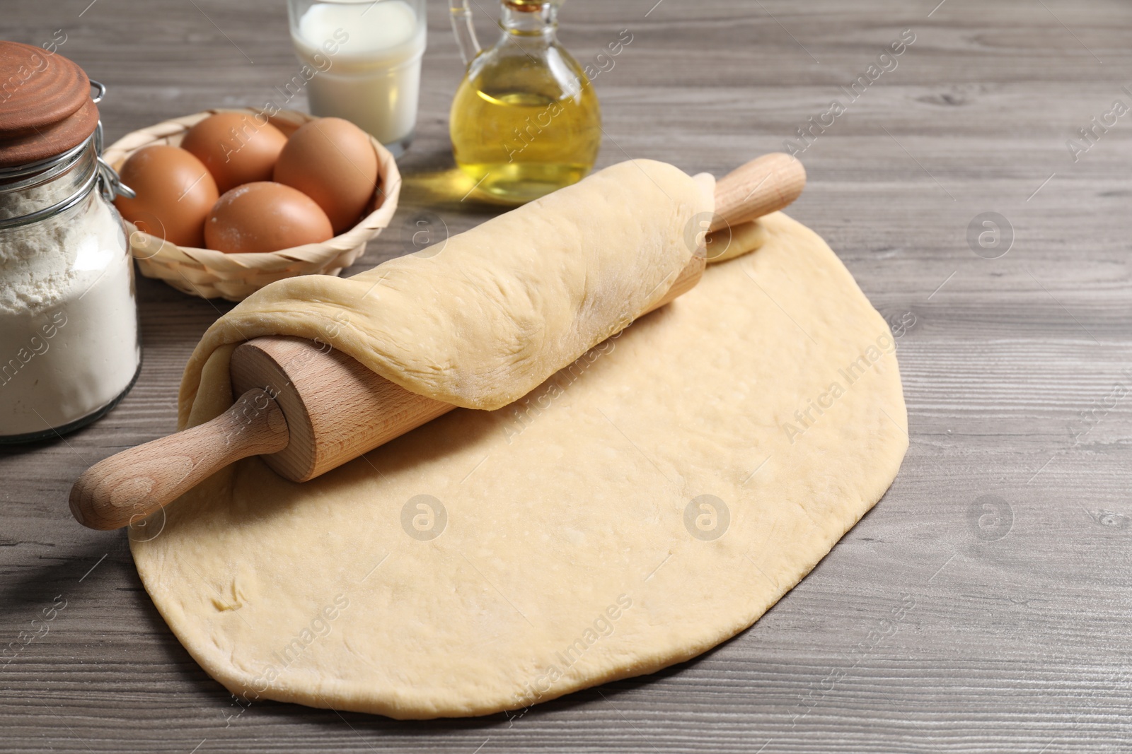 Photo of Raw dough, rolling pin and ingredients on wooden table