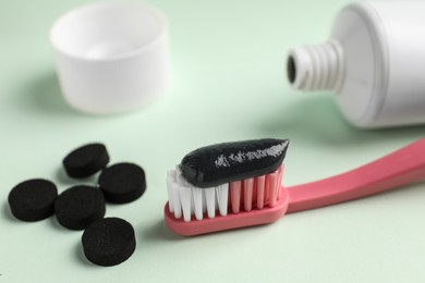 Photo of Brush with charcoal toothpaste and tablets on white background, closeup