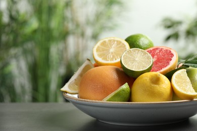 Photo of Different fresh citrus fruits on grey table against blurred background, closeup. Space for text