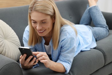 Happy woman sending message via smartphone on couch at home